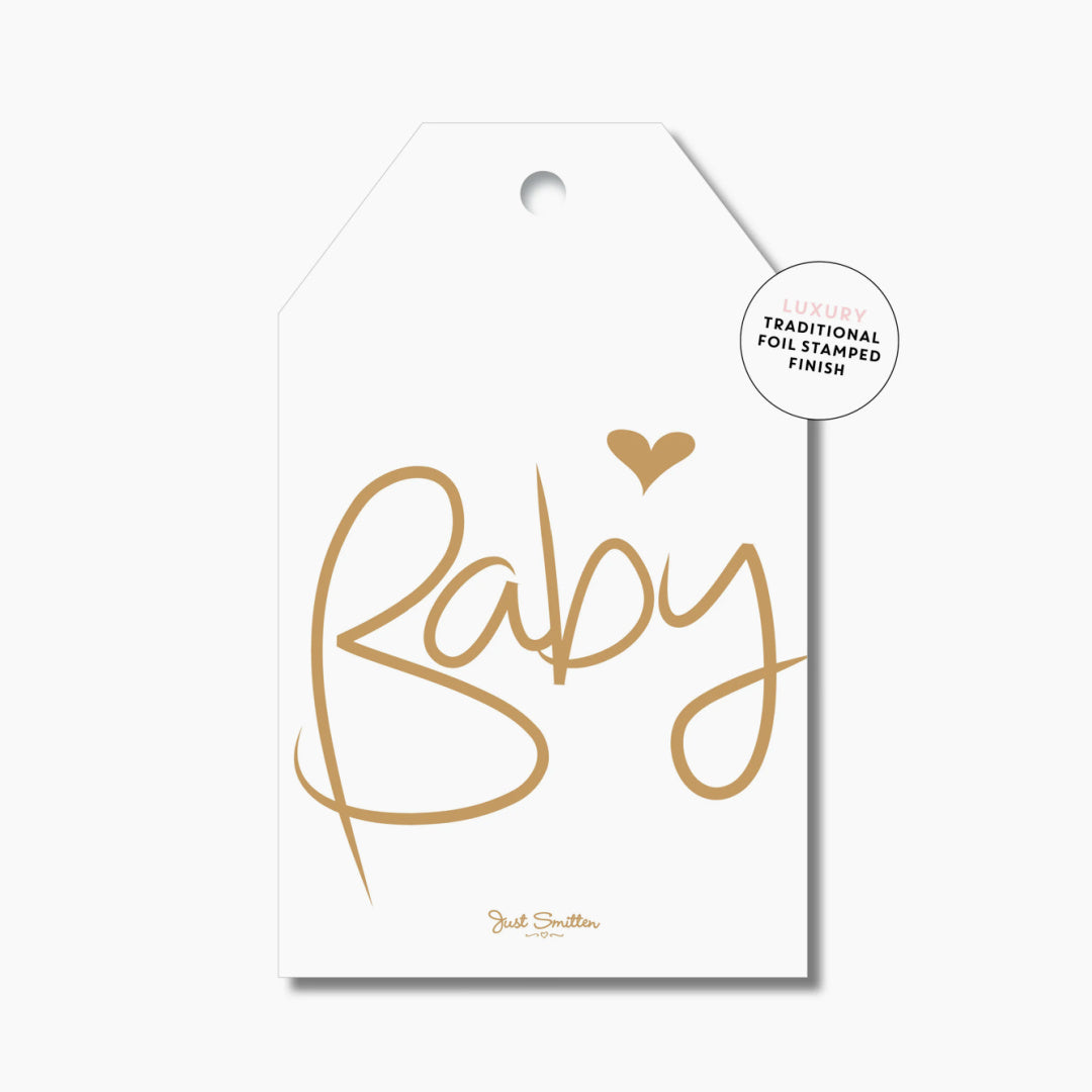 A white gift tag with the word 'Baby' written in gold foil, with a heart symbol above the word.