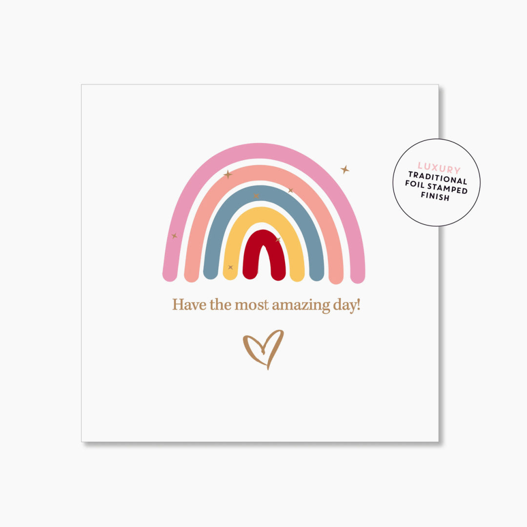 A greeting card with a colourful rainbow design and the text &#39;Have the most amazing day!&#39; features a heart shape, with a gold foil finish.