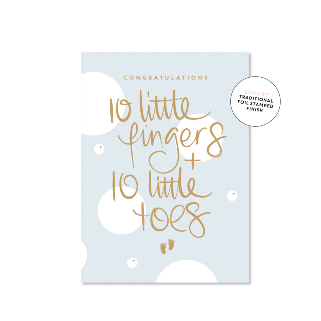 A blue luxury greeting card with gold foil text reading &#39;CONGRATULATIONS 10 LITTLE FINGERS + 10 LITTLE TOES&#39; with a small pair of footprints below the text.